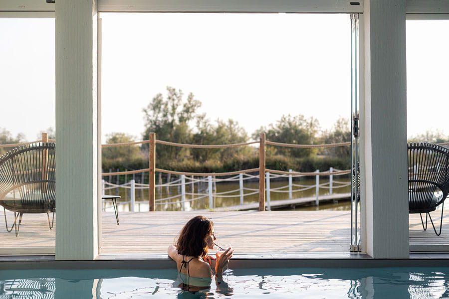 Femme dans une piscine intérieure devant une large baie vitrée donnant sur la Camargue